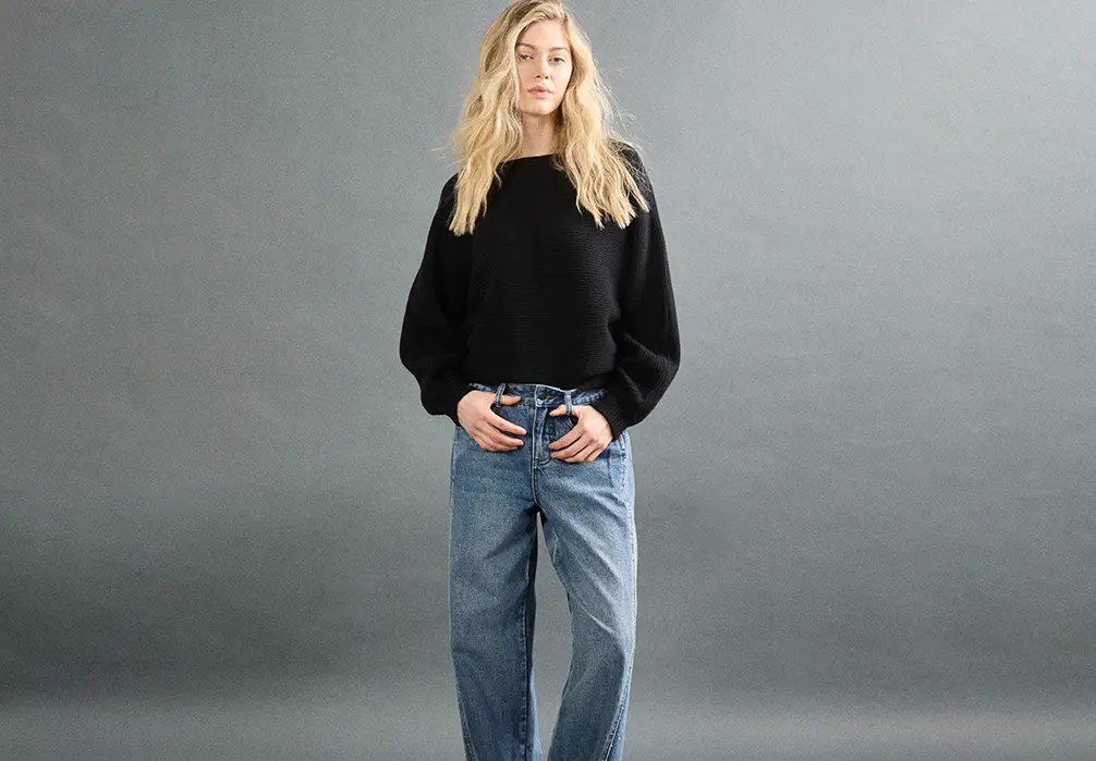 The model is wearing a baggy black knitted sweatshirt with baggy blue jeans with sparkle detailing