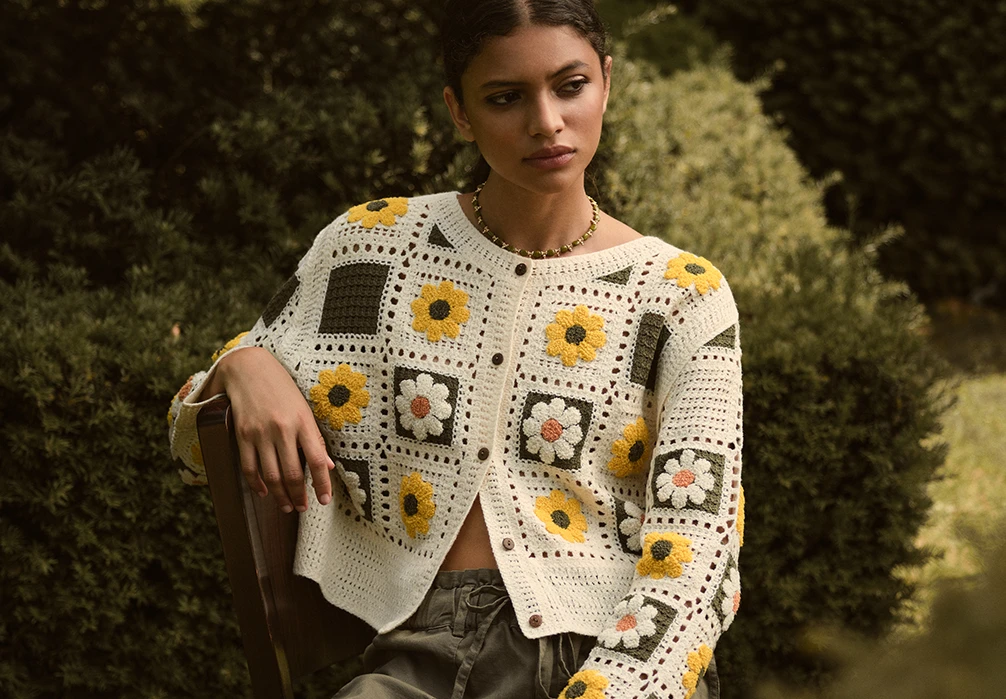 A girl standing in a dress. Text on image: Discover comfort & style with our collection of new-in knitwear. On breezy evenings, cover up with lightweight layers - from crochet cardigans to waistcoats & vests designed for in-between days. As the weather cools, build your cold-weather rotation with knitted tops & cosy jumpers in classic cable & waffle knits. Layer your look with an oversized jumper, & keep the cold at bay with a warm fleece. Shop new-in women’s cardigans, jumpers, & knitwear made for now & later. 