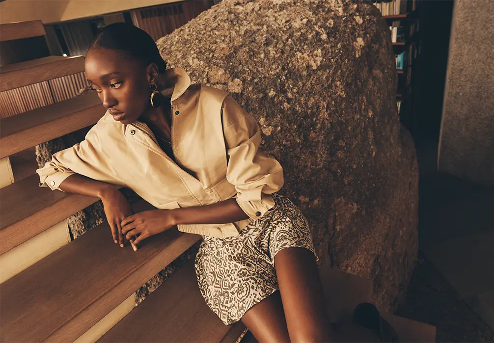 Model sitting on stairs wearing the Pleat Detail Bomber Jacketover a dress