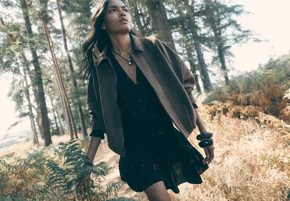 Model is wearing a Floral Print Smocked Mini Dress with a brown suede bomber jacket