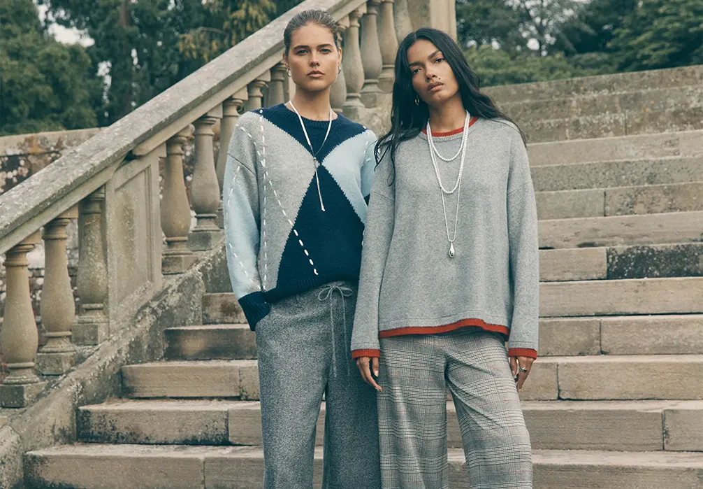 Two models standing wearing a a grey layered knitted sweater and a blue argyle jumper