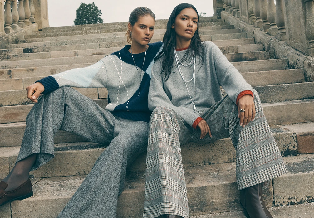 Two models are sat on the stairs wearing grey trousers