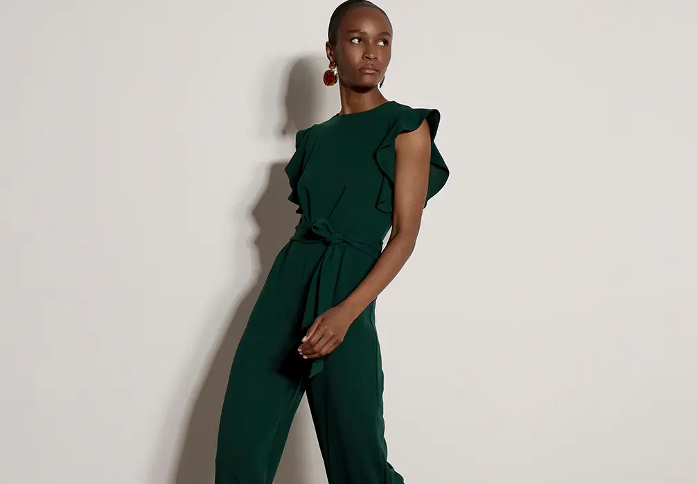 Models standing wearing an emerald green jumpsuit with a frilly sleeve