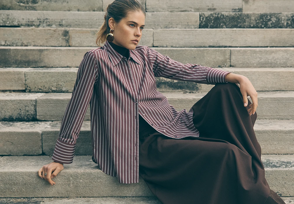 Model is sat down wearing a burgundy striped shirt 