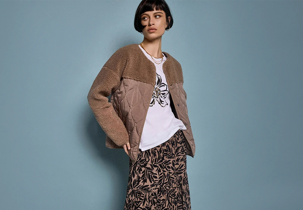 A girl standing in a coat. Text on image: Whatever the weather, explore new-in women’s coats & jackets. From lightweight layers designed for in-between days & chilly evenings, to winter coats made to keep the cold at bay, update your wardrobe with our year-round outerwear heroes. Elevate your workwear wardrobe with a smart tailored peacoat, or keep it casual with a cosy puffer jacket that combines comfort & warmth. Discover luxe faux fur coats & leather jackets that will take you from day to after dark in style. Get set for rainy days, city strolls & everything in between with raincoats, practical parkas, & quilted jackets. No wardrobe is complete without a timeless denim jacket. Shop new-in women’s coats & jackets now.