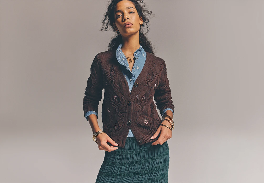 Model is wearing a denim shirt with a brown knit embroided cardigan buttoned up