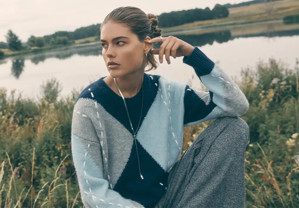 Studio shot of model wearing a blue argyle knitted sweatshirt