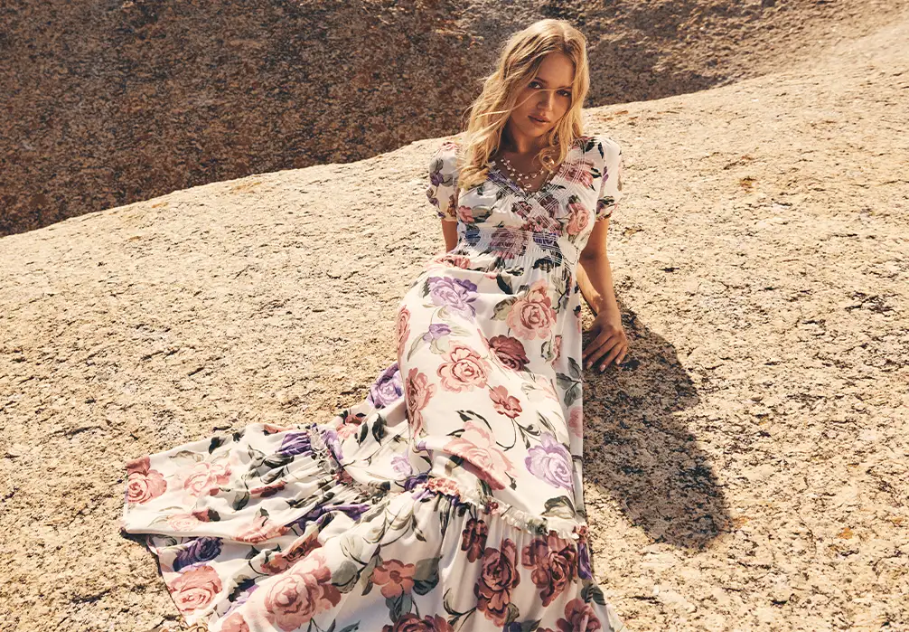 Model wearing floral Maxi dress lying down on a boulder