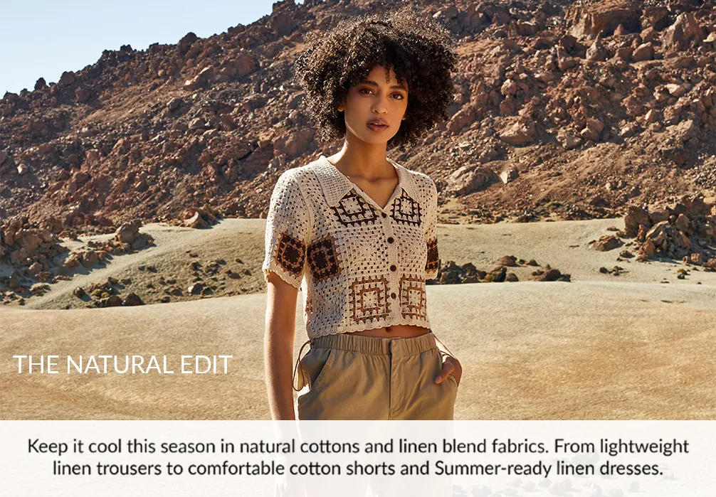 A girl standing in cotton crochet top. Text on image: Keep it cool in natural cottons and linen blend fabrics this season. From lightweight linen trousers to comfortable cotton shorts and summer-ready linen dresses.